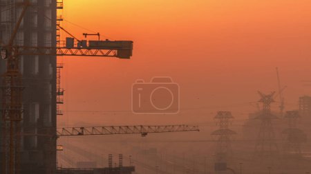 Photo for Building of new modern skyscrapers under construction timelapse during sunrise and power lines in futuristic city. Aerial view of roads with high traffic in Business Bay, Dubai, United Arab Emirates - Royalty Free Image