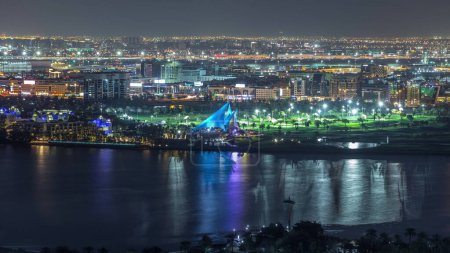 Téléchargez les photos : Terrain de golf dans la ville avec des lumières des bâtiments et des routes éclairées la nuit timelapse aérien près de la rivière dans Dubai Creek. Aéroport sur fond, Dubaï, Émirats arabes unis - en image libre de droit