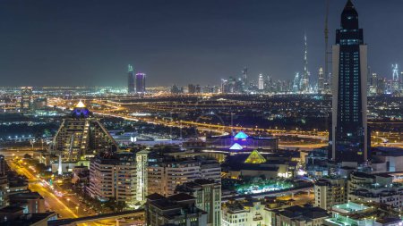 Téléchargez les photos : Vue aérienne des gratte-ciel éclairés de la ville avec des lumières des routes et du centre-ville sur fond de timelapse aérien la nuit depuis Dubai Creek, Émirats arabes unis - en image libre de droit