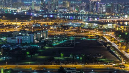 Traffic on roads and modern buildings at nighttime near river with lights from yachts in Deira Aerial Timelapse in luxury Dubai city, Dubai Creek, United Arab Emirates