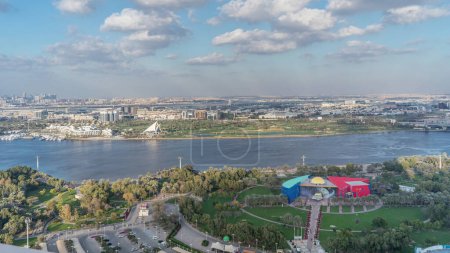 Panoramic view of park and golf course near blue river with reflections from water Aerial Timelapse at sunny day in Dubai Creek, United Arab Emirates
