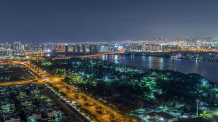 Téléchargez les photos : Rythme nocturne du panorama de la ville avec des gratte-ciel sur un fond la nuit près de la rivière dans Dubai Creek timelapse aérien. Parc et circulation sur les routes, Dubaï, Émirats arabes unis - en image libre de droit