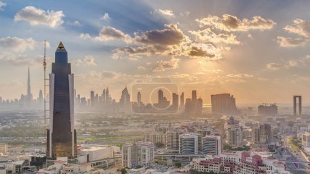 Foto de Puesta de sol sobre rascacielos del centro de la ciudad de lujo con reflejo en edificios modernos cerca de Dubai creek timelapse noche aérea con nubes de colores, Emiratos Árabes Unidos
. - Imagen libre de derechos
