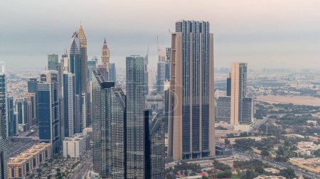 Téléchargez les photos : Dubai International Financial Centre district avec des gratte-ciel modernes de jour comme de nuit transition timelapse. Vue aérienne du centre-ville avec circulation dans les rues après le coucher du soleil - en image libre de droit