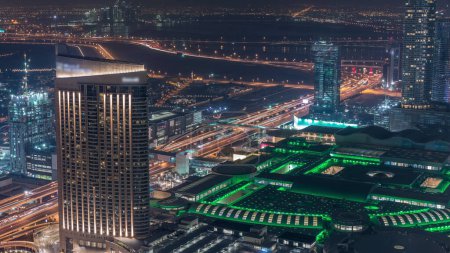 Téléchargez les photos : Vue aérienne imprenable sur les gratte-ciel du centre-ville de Dubaï timelapse nocturne avec centre commercial et la circulation sur l'autoroute, Dubaï, Émirats arabes unis. Tours modernes éclairées et chantier de construction - en image libre de droit