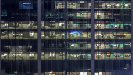 Photo for Office building exterior during late evening with interior lights on and people working inside night timelapse. Aerial close up view from above with many illuminated windows - Royalty Free Image