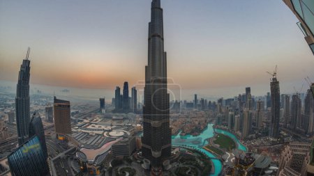 Téléchargez les photos : Vue panoramique sur l'horizon du centre-ville de Dubaï pendant le lever du soleil avec centre commercial, fontaines et Burj Khalifa nuit aérienne à la transition de jour timelapse. gratte-ciel modernes et ciel nuageux avant le lever du soleil - en image libre de droit