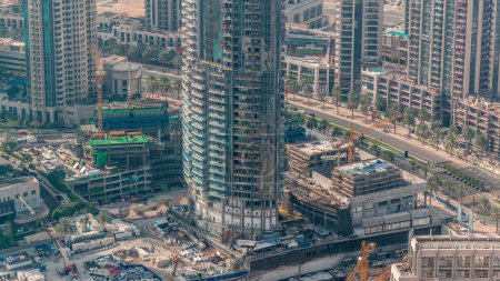 Téléchargez les photos : Bâtiment de grande hauteur en construction avec grue de construction jaune à Dubaï timelapse. Vue aérienne le matin dans le centre-ville. Sous-sol avec tracteurs et bulldozers - en image libre de droit