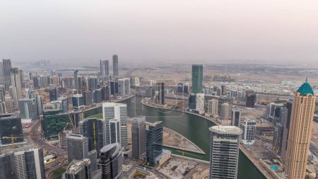 Photo for Panoramic aerial view of business bay towers in Dubai day to night transition timelapse. Rooftop view of some skyscrapers, canal and new towers under construction after sunset. - Royalty Free Image