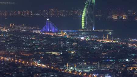 Téléchargez les photos : Vue aérienne des toits de la ville de Dubaï la nuit avec un hôtel burj al arab illuminé et un timelapse Palm Jumeirah. Vue depuis Business bay skyscraper, Dubai, Émirats arabes unis
. - en image libre de droit