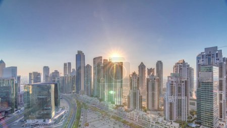 Photo for Modern residential and office complex with many towers aerial timelapse with sunset at Business Bay, Dubai, UAE. Bay Avenue Park near big parking lot with cars and traffic on roads - Royalty Free Image