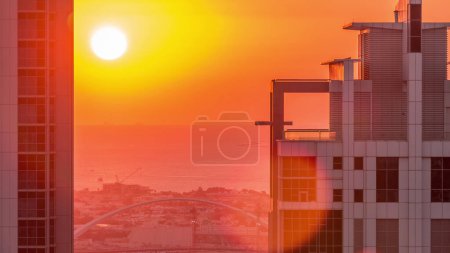 Foto de Puesta de sol detrás de un moderno complejo residencial y de oficinas en Business Bay, Dubai, Emiratos Árabes Unidos. Cielo naranja y canal de agua con puente sobre fondo - Imagen libre de derechos
