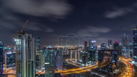 Téléchargez les photos : Vue aérienne des bâtiments éclairés timelapse pendant toute la nuit et circulation intense sur les routes près du canal. Vie nocturne à Business Bay, Dubai, Émirats arabes unis - en image libre de droit