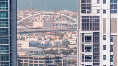 Photo for Pedestrian Bridge over the Dubai Water Canal aerial timelapse between towers in Business bay from above. Houses and traffic on the road - Royalty Free Image