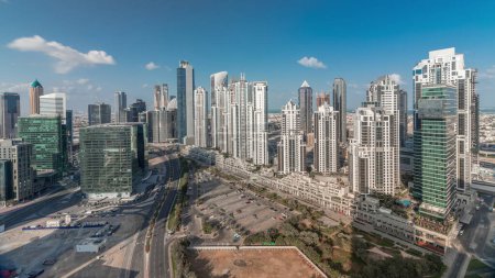 Photo for Modern residential and office complex with many towers aerial timelapse at Business Bay, Dubai, UAE. Bay Avenue Park near big parking lot with cars and traffic on roads. Clouds on a blue sky - Royalty Free Image