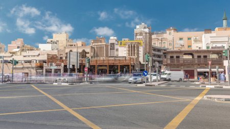 Foto de Tráfico en la intersección cerca de la entrada al timelapse de Gold Souk en Deira en Dubai, Emiratos Árabes Unidos. Antiguos edificios tradicionales con cielo nublado. Uno de los destinos de compras más populares - Imagen libre de derechos