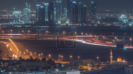 Téléchargez les photos : Construction de nouveaux gratte-ciel dans le port de Dubai Creek timelapse de nuit aérienne avec des tours éclairées. Dubaï - EAU. Vue de dessus du centre-ville de Dubaï avec circulation sur une autoroute - en image libre de droit
