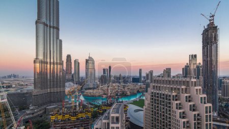 Foto de Skyline panorámico del centro de Dubái después de la puesta del sol con el centro comercial, fuentes y Burj Khalifa día aéreo a la noche timelapse transición. Rascacielos modernos y obras de construcción - Imagen libre de derechos