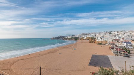 Foto de Panorama que muestra la amplia playa de arena y el océano Atlántico en la ciudad de Albufeira timelapse. Casas blancas en la cima de los acantilados. Vista aérea desde arriba. Nubes en un cielo azul. Algarve, Portugal - Imagen libre de derechos