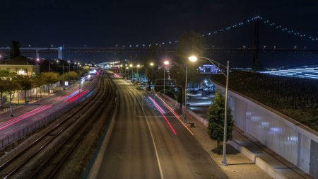 Night traffic view of India Avenue in Belem zone in Lisbon Portugal. Car light trails timelapse. Illuminated bridge on background
