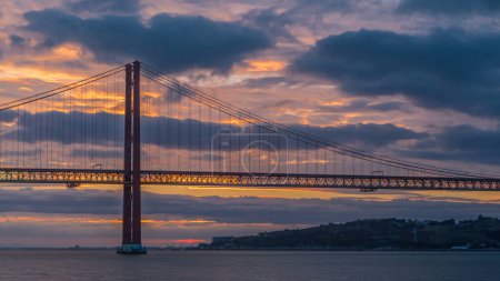 Lissabon Stadt Sonnenaufgang mit 25. April Brücke Zeitraffer, Fluss und Wasser am frühen Morgen. Orangefarbene Wolken am Himmel