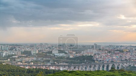 Photo for Lisbon and Almada during sunrise from viewpoint in Monsanto morning timelapse. Aerial top view with golden light, colorful clouds and rays of light. Aqueduct of the Free Waters and roofs of buildings - Royalty Free Image