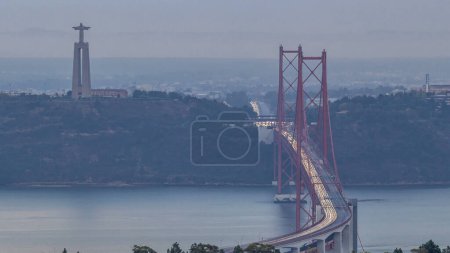 Lisbon and Almada during sunrise with traffic on April 25 bridge from a viewpoint in Monsanto at morning timelapse. Aerial top view with Cristo Rei monument. Foggy weather