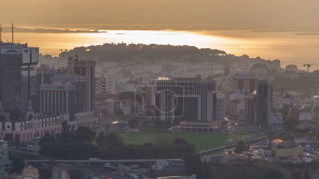 Lisbon during sunrise from viewpoint in Monsanto at morning timelapse. Aerial top view with golden light, colorful clouds and rays of light reflected on river surface and roofs of buildings