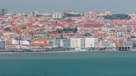 Panorama of Lisbon historical center aerial timelapse viewed from above the southern margin of the Tagus or Tejo River. Buildings with red roofs and floating ships on water