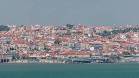 Téléchargez les photos : Panorama of Lisbon historical center aerial timelapse viewed from above the southern margin of the Tagus or Tejo River. Buildings with red roofs and floating ships on water near port - en image libre de droit