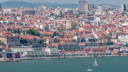 Panorama of Lisbon historical centre aerial timelapse viewed from above the southern margin of the Tagus or Tejo River. Buildings with red roofs and floating ships on water and cranes