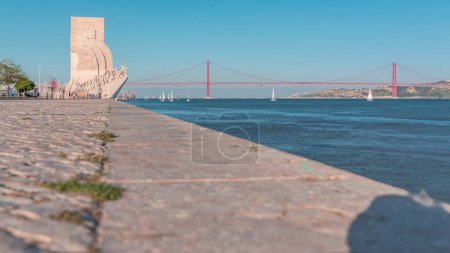 Foto de Padrao dos Descobrimentos (Monumento a los Descubrimientos) celebra a los portugueses que participaron en la Era del Descubrimiento timelapse, Lisboa, Portugal. Frente al mar con río y puente sobre fondo - Imagen libre de derechos