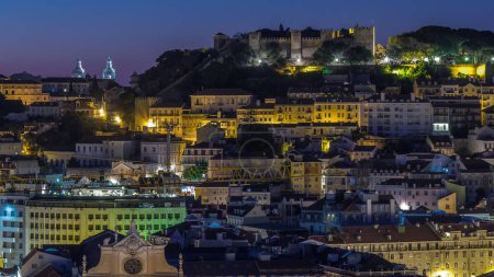 Photo for Lisbon aerial cityscape skyline night to day transition from viewpoint of St. Peter of Alcantara, Portugal. Illuminated historical buildings with Castelo de S. Jorge from above before sunrise - Royalty Free Image