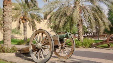 Foto de Fortaleza histórica en el Museo de Ajman timelapse hiperlapso con el cielo azul, Emiratos Árabes Unidos. Cañón viejo cerca de la palma - Imagen libre de derechos