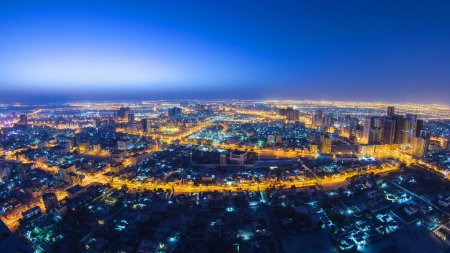 Panorama-Stadtbild von Ajman vom Dach aus von der Nacht zum Tag Übergang Zeitraffer vor Sonnenaufgang. Ajman ist die Hauptstadt des Emirats Ajman in den Vereinigten Arabischen Emiraten.