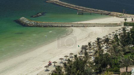 Schöner Strand mit Pier in Ajman Zeitraffer in der Nähe des türkisfarbenen Wassers des Arabischen Golfs, VAE. Panoramablick von der Dachterrasse auf die Küste