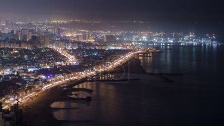 Foto de Vista panorámica de la costa de Sharjah por la noche desde la azotea de Ajman, la tercera ciudad más grande y poblada de los Emiratos Árabes Unidos. Sharjah se encuentra a lo largo de la costa norte del Golfo en la Península Arábiga - Imagen libre de derechos