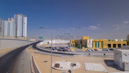 Foto de Tráfico por carretera en paso elevado en Ajman, vista desde el puente durante el día hiperlapso del timelapse aéreo. Paisaje urbano con torres sobre fondo en los Emiratos Árabes Unidos. - Imagen libre de derechos