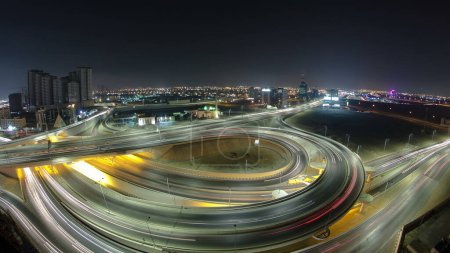 Foto de Tráfico en un gran cruce de carreteras en Ajman vista panorámica aérea desde la azotea por la noche timelapse. Muchos coches en intersección con el paso elevado en los Emiratos Árabes Unidos. - Imagen libre de derechos