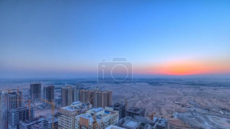 Foto de Paisaje urbano de Ajman desde la azotea durante el lapso de tiempo del amanecer. Vista panorámica aérea al nuevo distrito en construcción. Emiratos Árabes Unidos. - Imagen libre de derechos