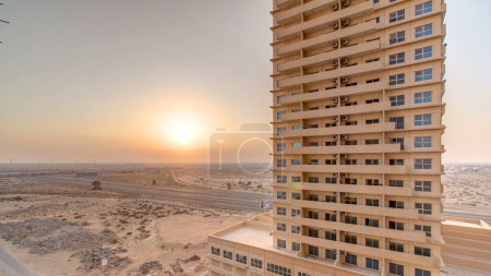 Foto de Puesta de sol en Ajman vista aérea desde timelapse azotea. Vista nocturna del sol en el cielo nublado naranja detrás de una torre residencial en los Emiratos Árabes Unidos. - Imagen libre de derechos