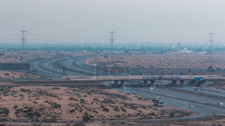 Foto de Carreteras en el desierto con tráfico día a noche timelapse transición en una gran ciudad de Ajman a Dubai después de la puesta del sol. Concepto de transporte. Vista desde arriba - Imagen libre de derechos