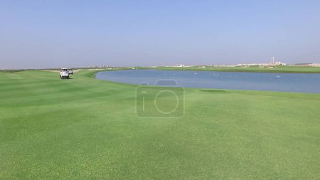 Téléchargez les photos : Vue aérienne d'un terrain de golf avec voiturette de golf se déplaçant sur la pelouse verte près de l'étang - en image libre de droit