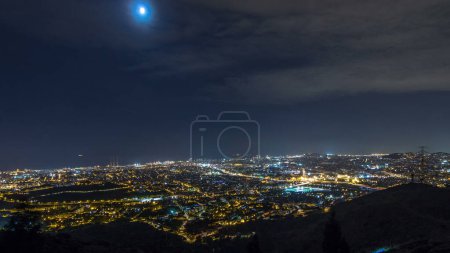 Nachtzeitraffer von Barcelona und Badalona Skylines. Luftaufnahme vom Aussichtspunkt Puig Castellar, beleuchtete Häuserdächer und das Meer am Horizont unter dem Sternenhimmel
