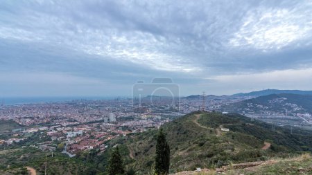 Day to Night Timelapse of Barcelona and Badalona Skylines. Aerial View from Iberic Puig Castellar Village Viewpoint, Showcasing Roofs of Houses and the Sea on the Horizon, as the Cityscape Transforms