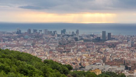 Foto de Barcelona 's Morning Palette: Sunrise Timelapse Panorama from the Bunkers of Carmel in Spain (en inglés). Vista superior aérea, rayos de luz rompen a través de las nubes, lanzando un colorido lienzo sobre el paisaje urbano moderno - Imagen libre de derechos