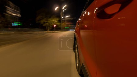 Téléchargez les photos : Drivelapse de côté de la voiture rapide se déplaçant sur une avenue de nuit dans une hyperlapsus timelapse ville, route avec des lumières réfléchies sur la voiture à grande vitesse. Rythme rapide d'une ville moderne. Mouvement flou - en image libre de droit