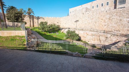 Téléchargez les photos : Mur défensif de l'antique hyperlapsus intemporel de Jérusalem, éclairé par le soleil. Magnifique pelouse verte avec des gens assis dessus - en image libre de droit