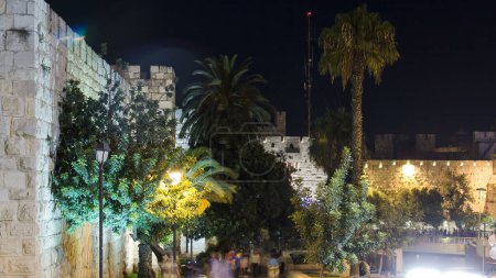 Foto de Murallas de la Ciudad Antigua por la noche timelapse, Jerusalén, Israel. Caminando por la calle con árboles verdes y palmeras. Iluminación nocturna - Imagen libre de derechos