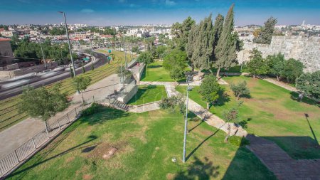 Téléchargez les photos : Vue de dessus du mur à Jérusalem Vieille ville timelapse avec le tramway moderne et la circulation sur la route. Jérusalem, Israël. Pelouse verte et ciel bleu - en image libre de droit